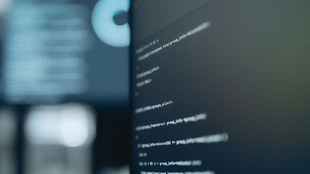 Close-up computer screen with programming code in dark office, showing software development and cybersecurity.
