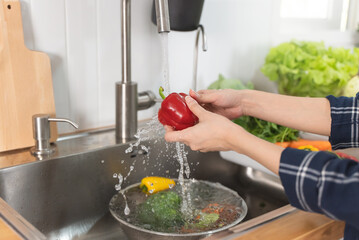 Obraz premium Close up of hands people washing vegetables by tap water at the sink in the kitchen to clean ingredient prepare a fresh salad.