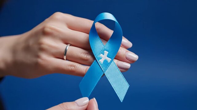 Blue Ribbon for Prostate Cancer Awareness - A close-up shot features a hand holding a light blue ribbon, the symbol for prostate cancer awareness. The background is a solid, matching blue color.