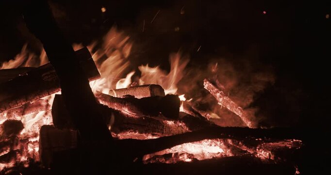Close-up view of burning firewood and flames in a bonfire at night.