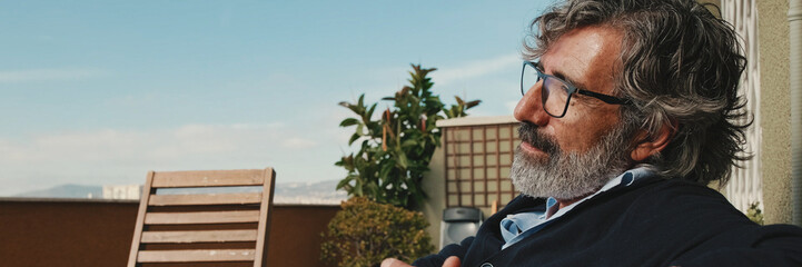 Naklejka premium Middle-aged man enjoying sunny weather on the balcony. Panoramic