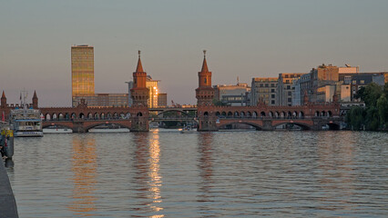 Obraz premium Brick gothic Oberbaum bridge over river Spree and apartment buildings in the evening sun with reflections in the water Berlin, Germany