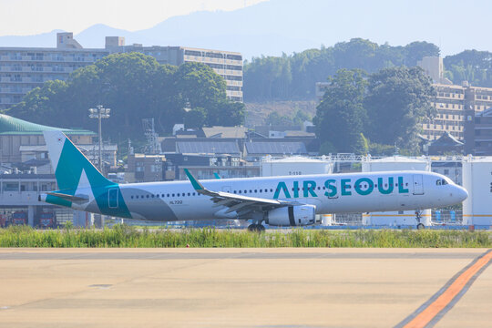 Fukuoka Japan - 2025 August 14: An Air Seoul Airbus A321 (HL7212) taxiing on the runway after landing at Fukuoka Airport with buildings and mountains in the background.