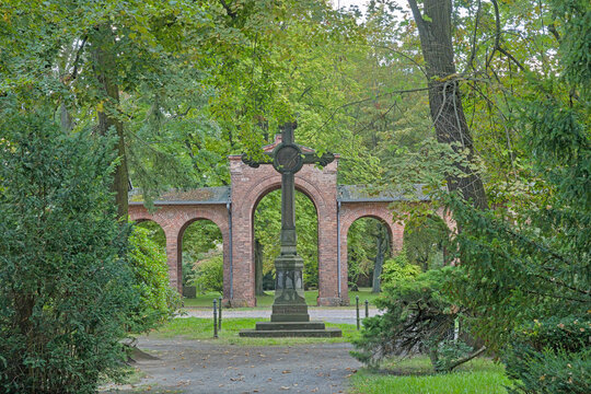  Cross and arcade surrounded by trees in Columbiadamm cemetery in Berlin, Germany 