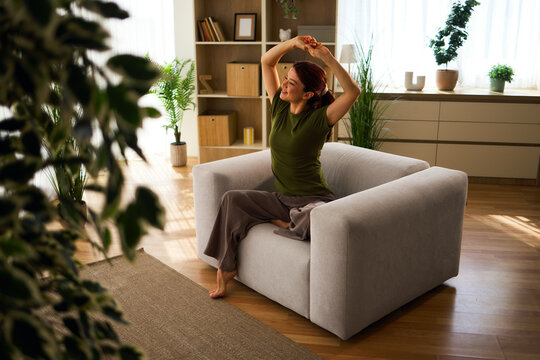 Happy woman enjoying peaceful morning at home in comfortable armchair