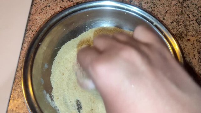 Hand breading raw pork chop in breadcrumbs inside metal bowl