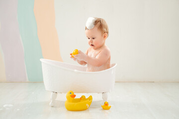 Naklejka premium a baby bathes in a tub with foam and rubber ducklings, the concept of child hygiene, a small child boy plays in a tub with foam or washes