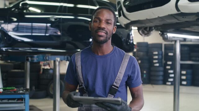 Portrait of African American mechanic using a tablet to diagnose breakdowns, check maintenance, and order parts, next to lifted cars