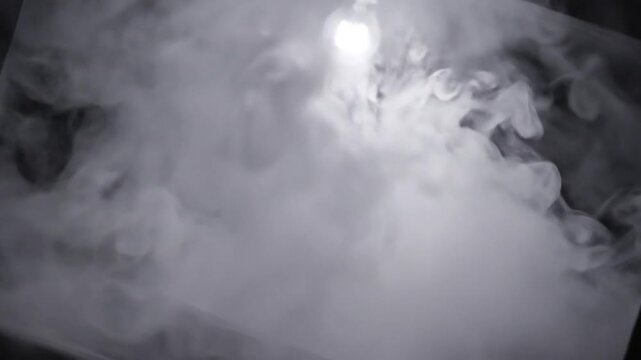 Abstract slow motion of smoke swirling in a dark studio, illuminated by a single overhead light