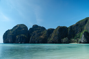 Obraz premium Serene view of tropical beach with clear turquoise water and towering limestone cliffs under bright blue sky