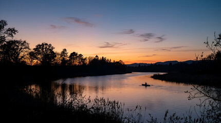 Obraz premium A solitary person kayaking on a calm river during a vibrant sunset.