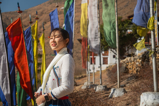 Portrait of a smiling Asian woman traveler holding a action vlog camera, standing against the background of a traditional Bhutanese building and rugged mountains in Bhutan