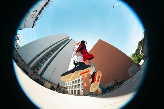 A basketball player jumps to dunk on an outdoor court, captured from a unique fisheye perspective. Buildings and a clear sky frame the action.