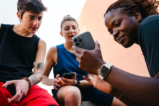 Three diverse young adults are gathered outdoors, intently looking at a smartphone screen. They are sharing content and enjoying a digital connection.