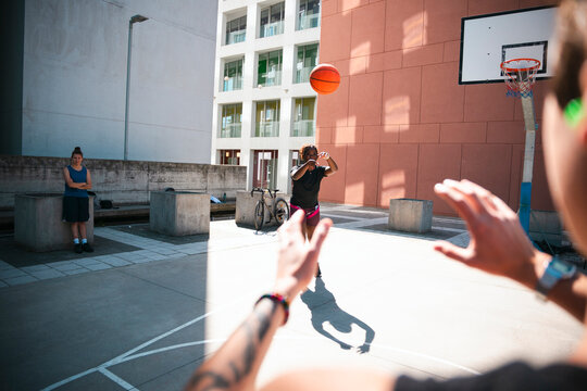 Three people enjoy a game of basketball on an outdoor court. One player throws the ball towards another, ready to receive it. A third person observes the action.