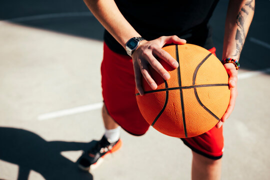 A person holds a basketball with both hands on an outdoor court. This player embodies an active lifestyle and passion for sports, ready for practice or a game.