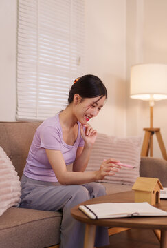 young Asian women sitting on sofa holding pink pen thinking planning writing notes studying working from home in cozy modern living room apartment with natural