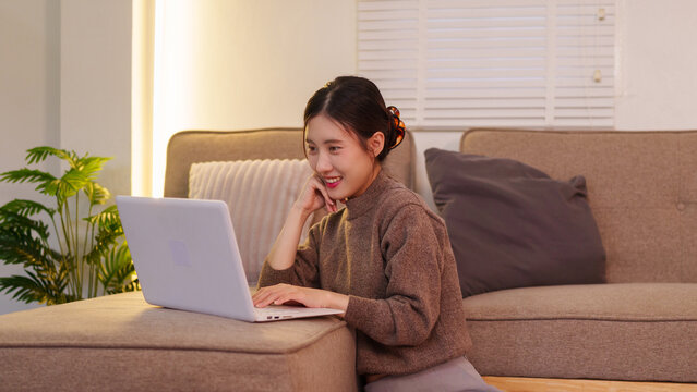 young asian women working on laptop computer sitting comfortable on sofa at home office remote work from home freelancer using technology browsing internet