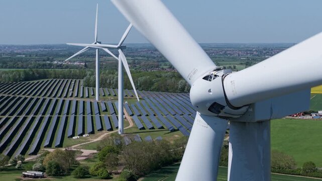 Close up aerial drone shot of a rotating wind turbine over a huge solar power plant hybrid energy farm UK