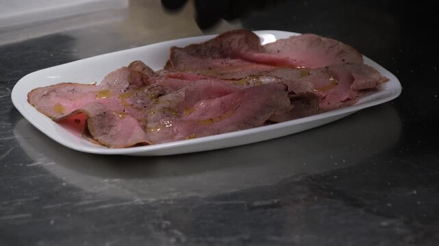 Preparazione di un piatto di roastbeef a fette. Condimento prima del servizio in una cucina di un ristorante