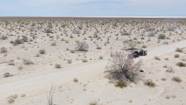 Aerial view shows an SUV with a teardrop camper trailer traveling across the Baja desert near El Salar salt flats in California.