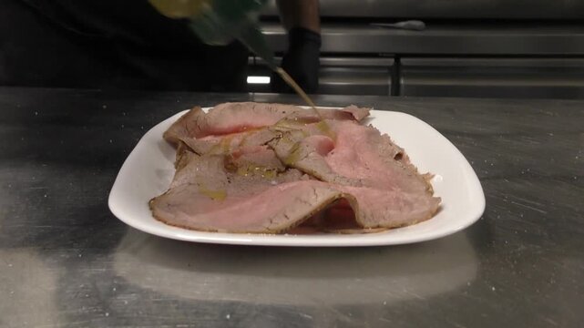 Preparazione di un piatto di roastbeef a fette. Condimento prima del servizio in una cucina di un ristorante