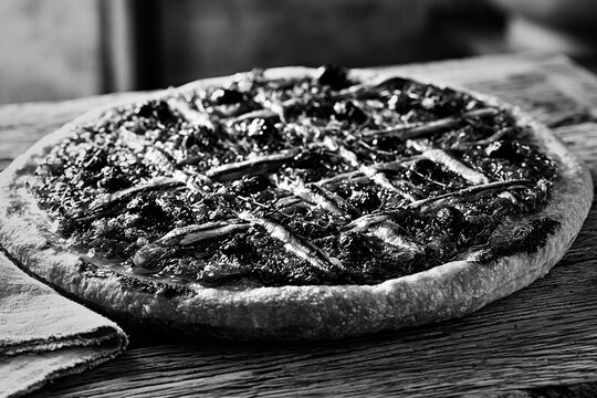 Traditional pissaladiere pizza with anchovies and olives on rustic woo