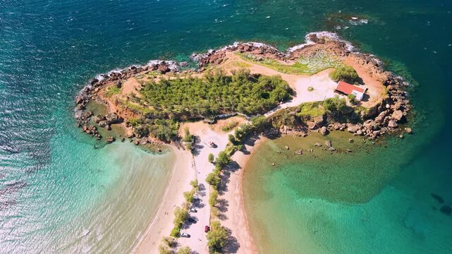 Agii Apostoli Double Beach Crete Greece low aerial view of white chapel on peninsula, emerald sea and rocks, drone orbit around church on Greek island Chania coast cinematic travel video for tourism