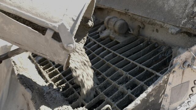 Concrete pouring from the chute of a mixer truck into a grate at a construction site, a crucial step in building a solid foundation for new real estate development under the bright sun
