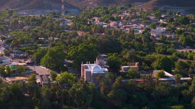 View aerial perspectives of the Mission Church in San Ignacio, Baja California. The church sits in a vibrant oasis town with greenery.