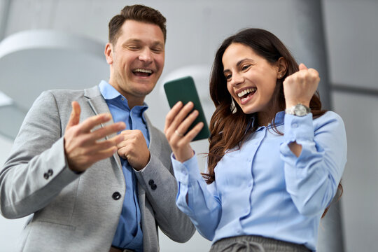 Cheerful  business colleagues celebrating good news received over smartphone  in a hallway.