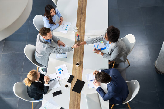 High angle view of business colleagues shaking hands across conference table on a meeting in the office