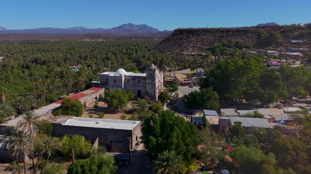 View aerial shots of Mission Church in San Ignacio surrounded by palm trees and desert landscape in Baja California, Mexico.
