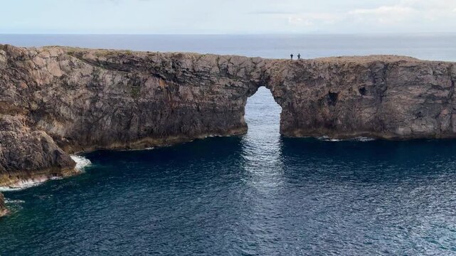 Two people enjoying the view from the impressive Pont d'en Gil natural rock bridge in Menorca.