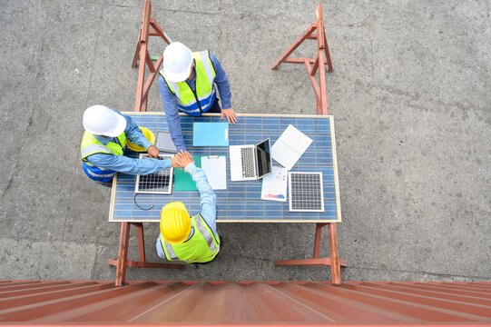 Top view of engineering team wearing helmets and safety vests discussion and brainstorming meeting for solar photovoltaic cell project. agreement for green alternative energy concept.