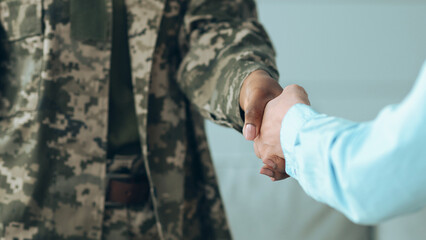 Fototapeta na wymiar Two individuals shake hands in a friendly manner. One person wears a military uniform, while the other is in casual clothing. The setting appears to be indoors, possibly during a community event.
