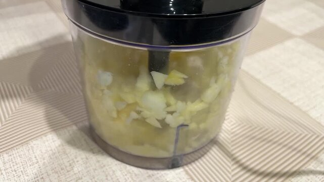 Mini chopper cutting apple pieces. Small kitchen device dicing apple sections within plastic bowl. Tiny chopper swiftly shredding apple slices into larger pieces inside storage container