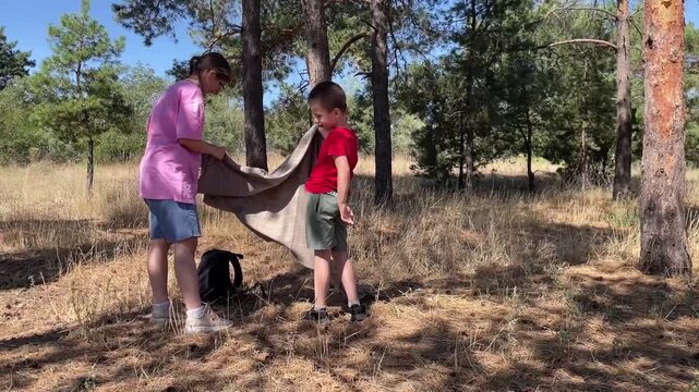 Kids craft tiny shelter outdoors, Youthful helpers assemble small structure in sunlit forest clearing, Children participate in building cozy miniature shelter amid pine trees with joyful enthusiasm