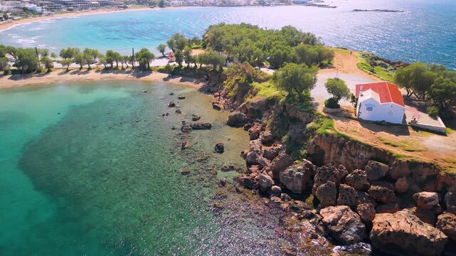Agii Apostoli Beach Crete Greece low aerial view of white chapel on peninsula, emerald sea and rocks, drone orbit around church on Greek island Chania coast cinematic travel video