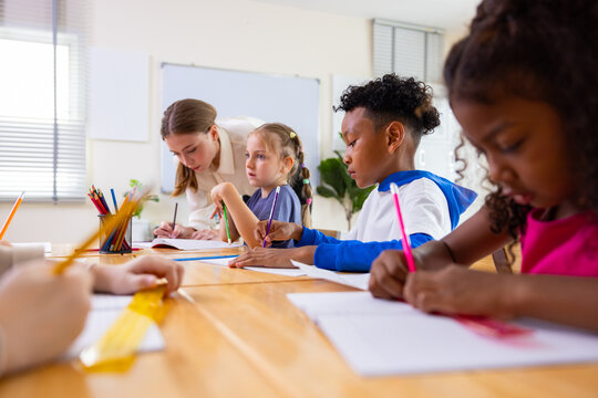 Teacher Helping Children Study Together in Classroom