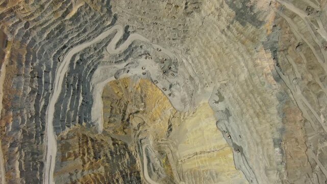 Aerial tilt view of open pit copper ore mine and heavy mining equipment. Excavator and mining trucks in quarry, 4k