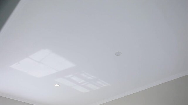 Minimalist white ceiling with recessed downlights and natural window reflection, 4K interior video.