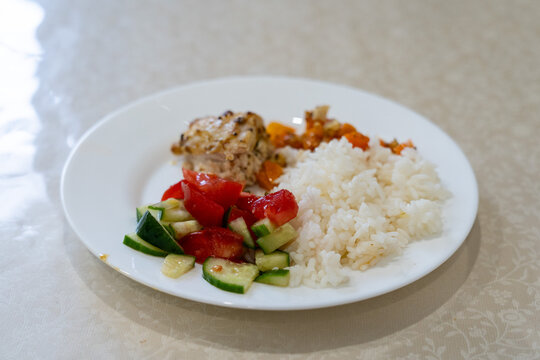 A Delicious Plate of Grilled Chicken, Fresh Vegetables, and Fluffy White Rice Served on a Simple White Dish