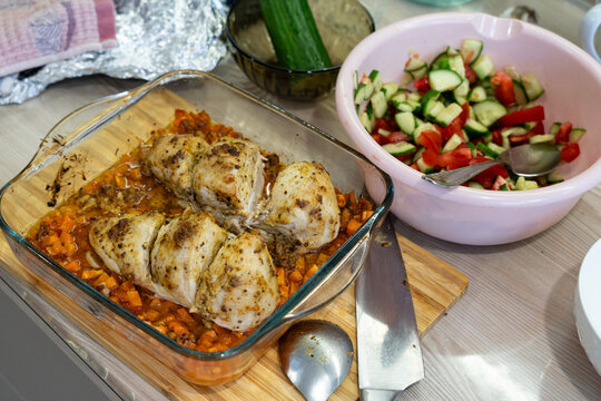 Deliciously Seasoned Baked Chicken Breasts on a Wooden Cutting Board Accompanied by Fresh Vegetable Salad and Condiments in a Kitchen Setting