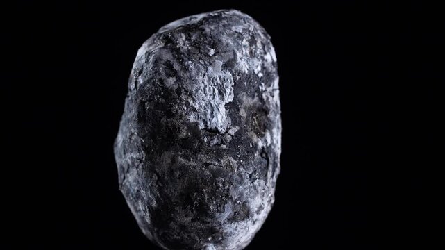 Single baked potato in skin isolated on black background. Macro view of a whole potato baked in coals split open to show fluffy yellow texture. Rustic organic food concept isolated on black, close up