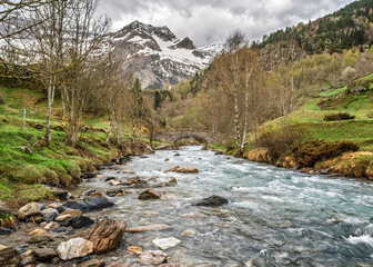 The Gave de Gavarnie river cascades down from the snow covered Cirque de Gavarnie through an ancient stone bridge in the French Pyrenees © Jon Ingall