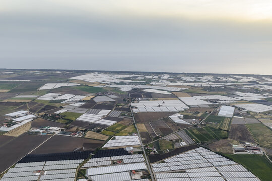 Aerial view of a vast agricultural landscape with numerous greenhouses and cultivated fields under a hazy sky in Paestum, Campania, Italy.