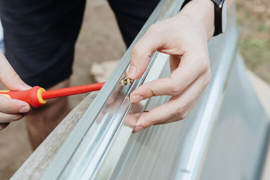 An unidentified assembler uses a screwdriver to screw a screw into a small bolt, installing a metal barn.