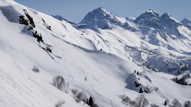 Majestic snow covered mountains standing tall against clear blue sky on bright winter sunny day. Revealing vast and pristine alpine wilderness with ski tracks visible on slopes