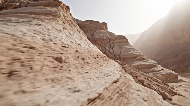 Wide shot of pale stratified rock formations and layered sandstone hills in a barren arid desert landscape with a dust cloud moving through a narrow canyon under bright sun.